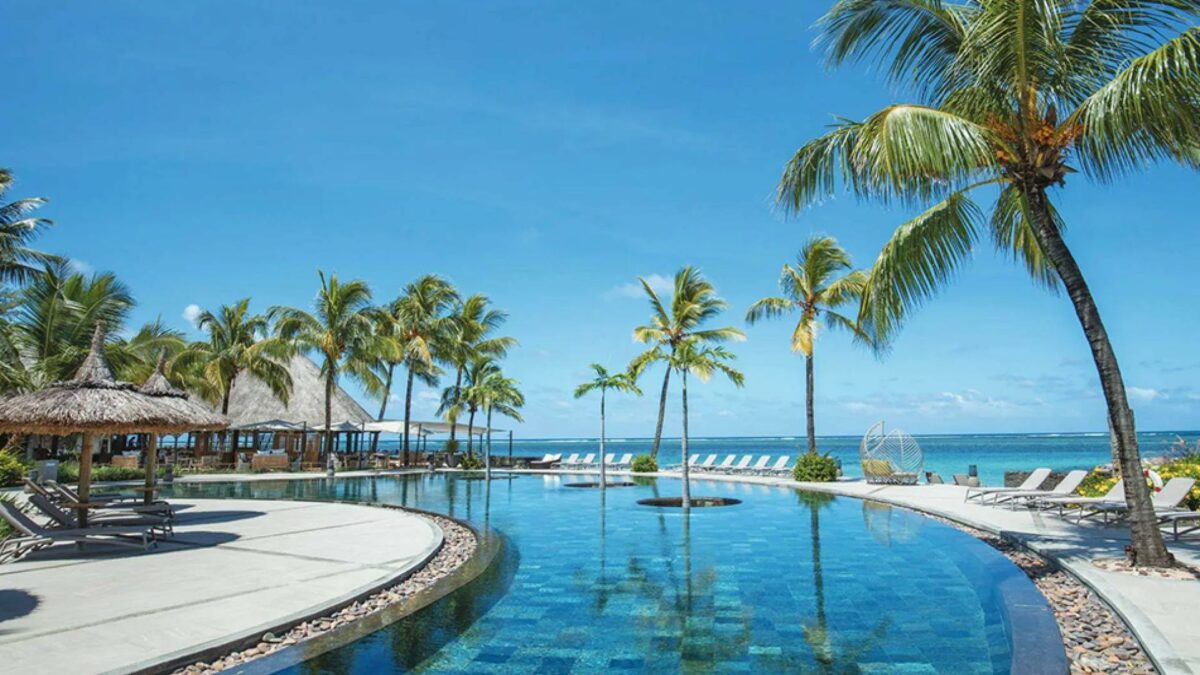 Holiday resort in Thailand showing a blue lazy river pool with pool chairs overlooking the crystal blue ocean. This is Mauritius on a budget. 
