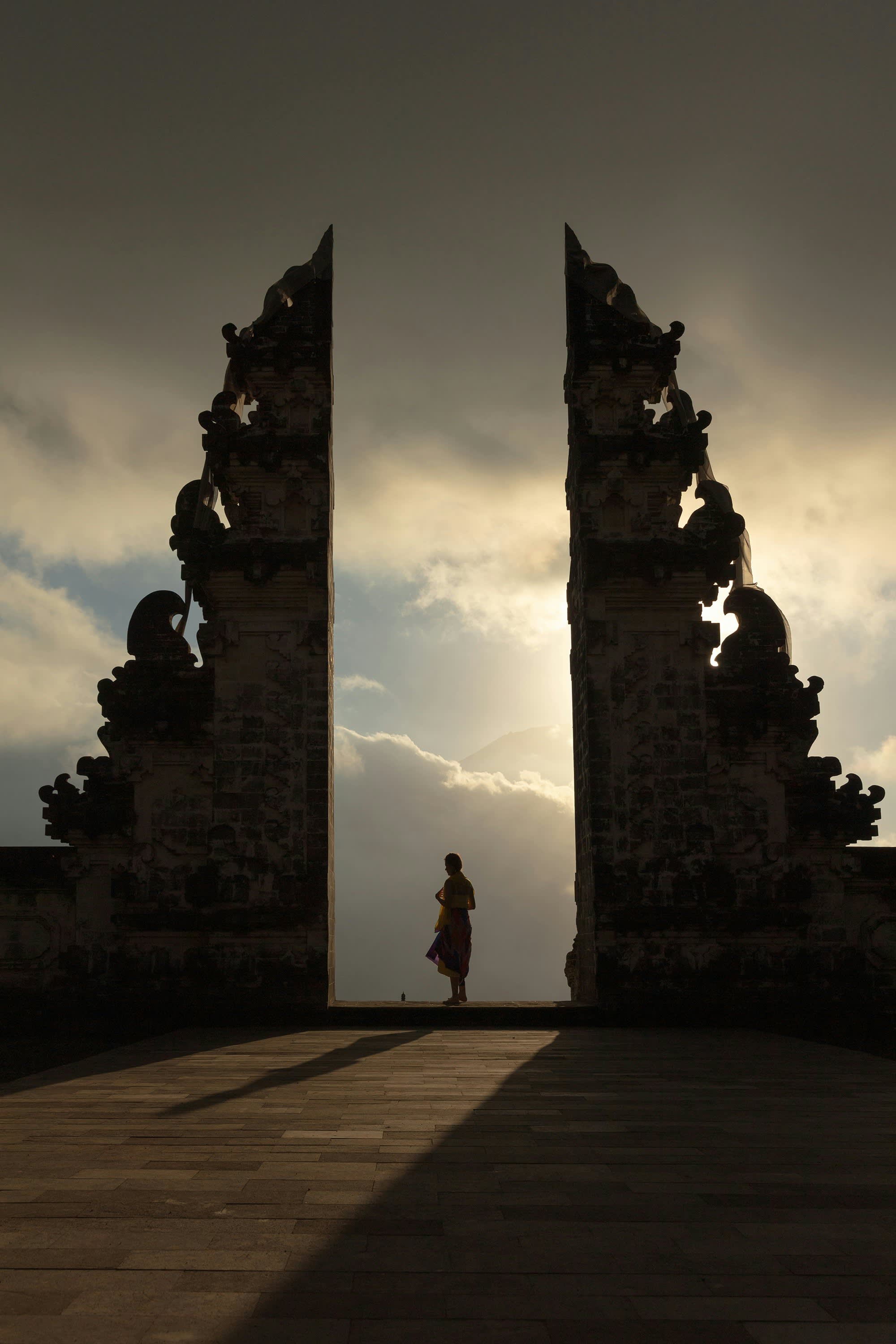 Silhouette of a person standing in the split gateway of Bali's Lempuyang Temple against a dramatic cloudy sky.