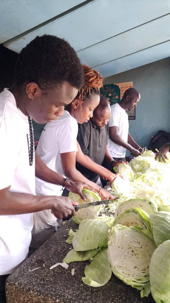 Volunteers chopping large heads of cabbage at a table during ETAfrica Volunteer Day 3 food service activity.