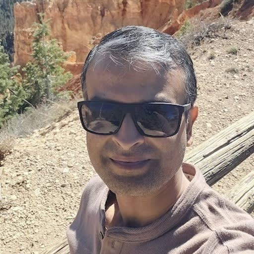 Man wearing sunglasses taking a selfie at a red rock canyon landscape, likely Bryce Canyon.