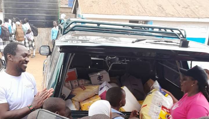Volunteers unloading food donations from a vehicle, surrounded by excited schoolchildren in uniforms during an ETAfrica community outreach day.