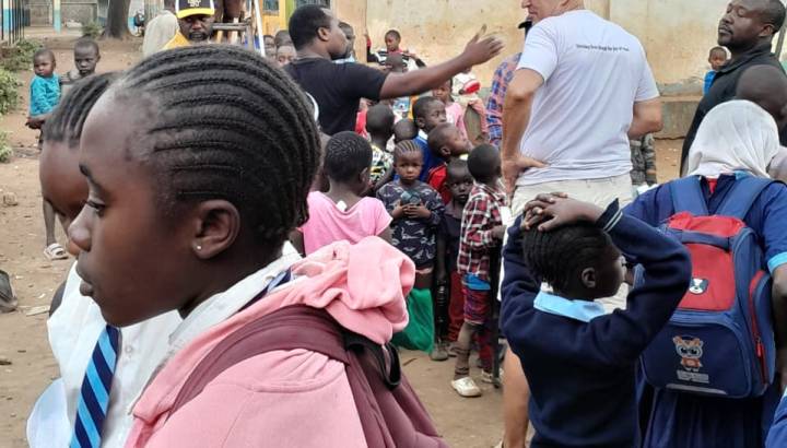 Volunteer in white shirt engaging with a large group of children and adults outside a school building in Africa.