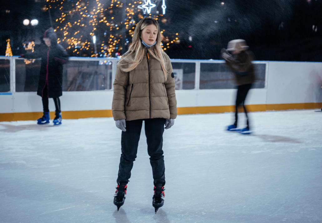 A blonde teenage girl skating on the skating rink with Christmas lights on the background