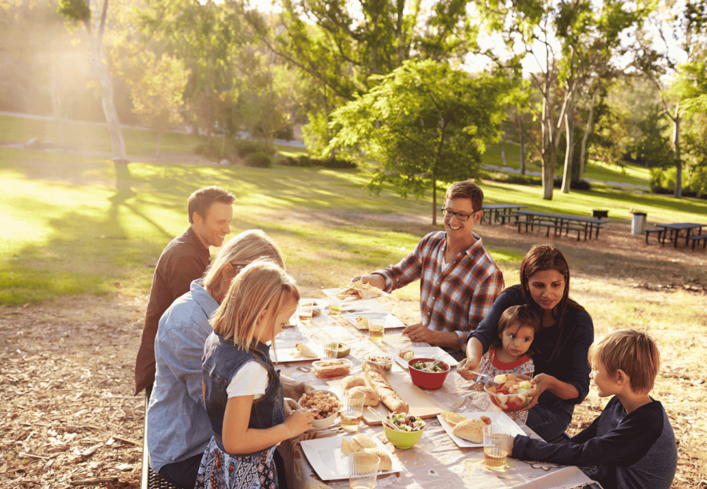 Two families having a picnic together at a table in a park