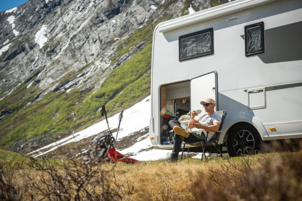 Tourist in Front of His Motor Home Taking Short Break to Eat Some Food on Fresh Air