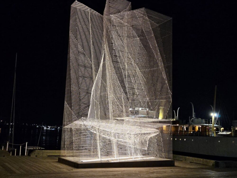 A very large sculpture on the dock made of wire with lighting that reveals a ship within it.