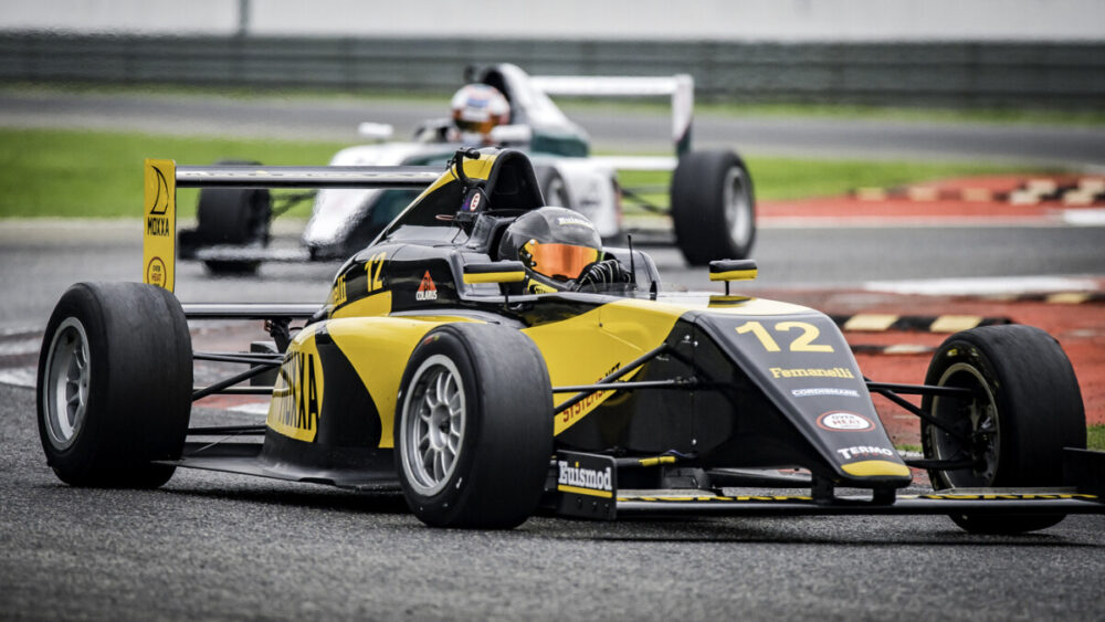 Black and yellow formula race car on the track trailed by another race car.